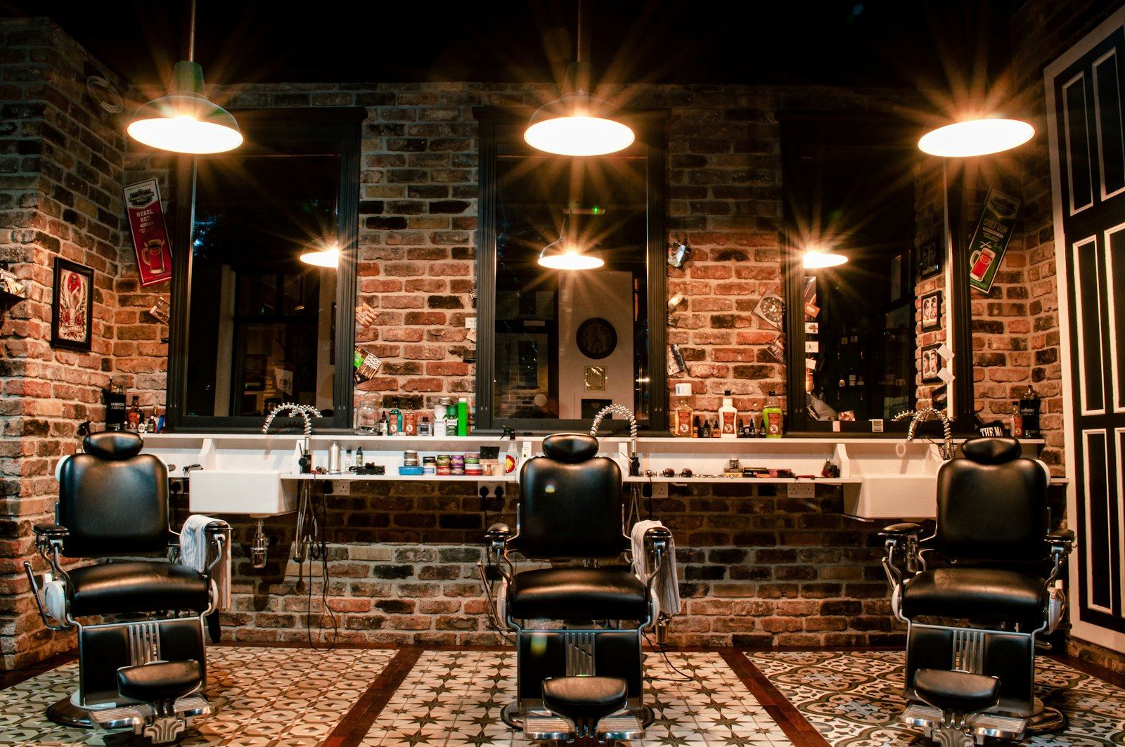 Three leather barber chairs in front of mirrors on a brick wall