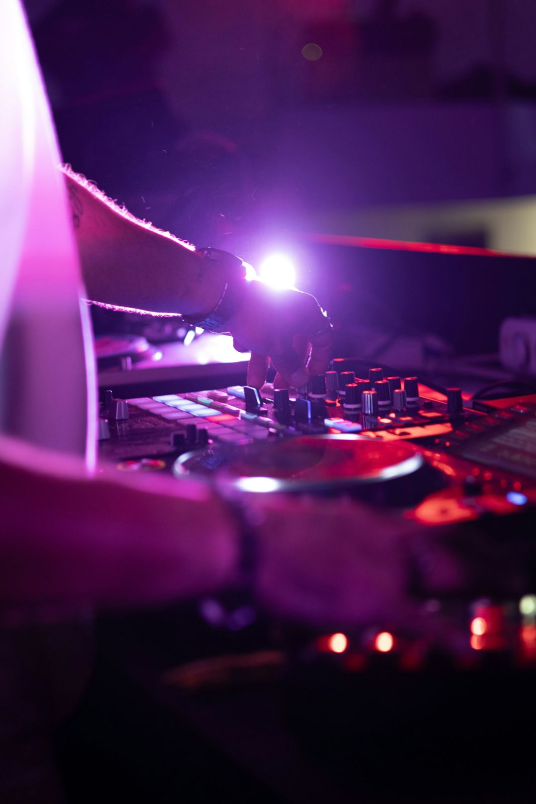 A DJ's hands on decks in purple light