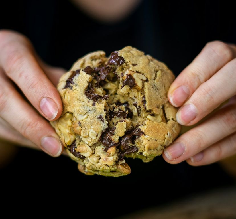 A walnut chunk cookie broken open in a baker's hands